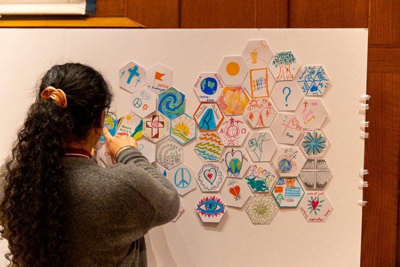 A student places a tile on a wall at an Interfaith Dinner event held early in 2020. These tiles represent individual worldviews